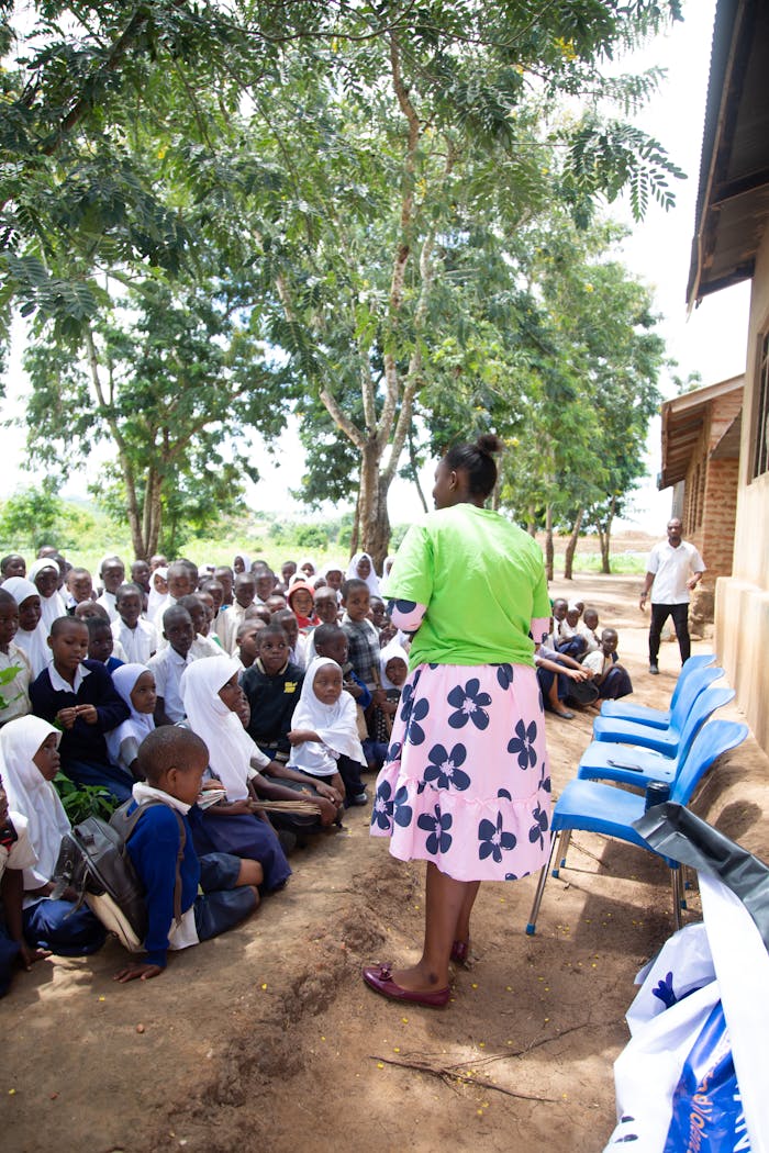 Teacher conducts outdoor lesson with attentive children under trees.