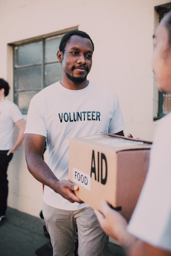 gallery-2 A volunteer hands a box labeled 'aid' and 'food' during an outdoor charity event.