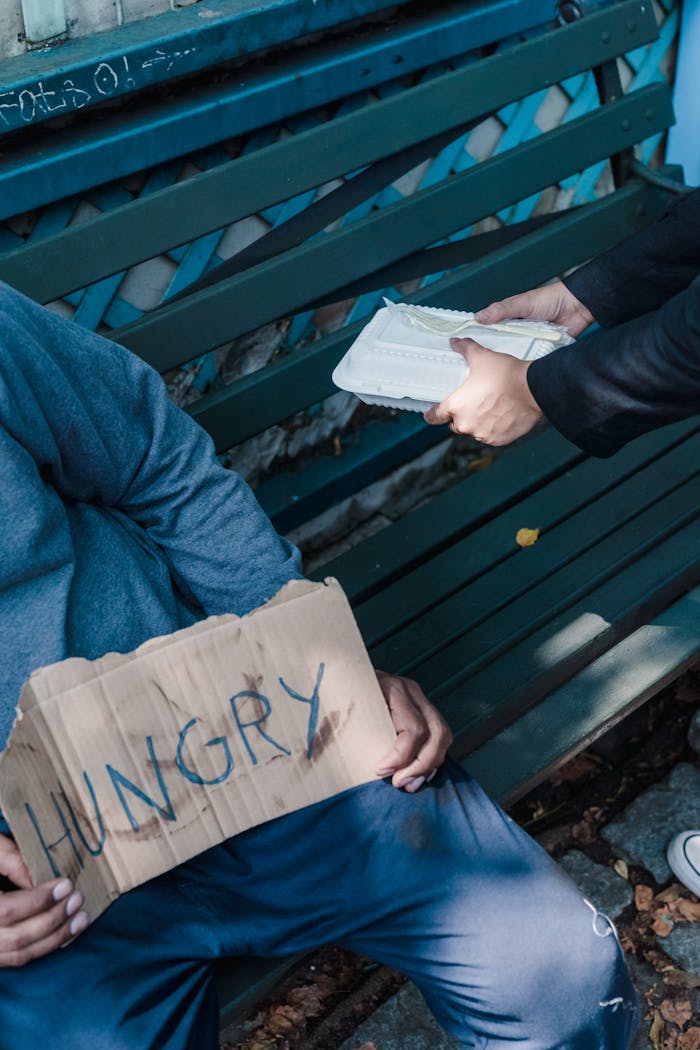 about-02 A person helps a homeless individual with food, illustrating kindness and poverty awareness.